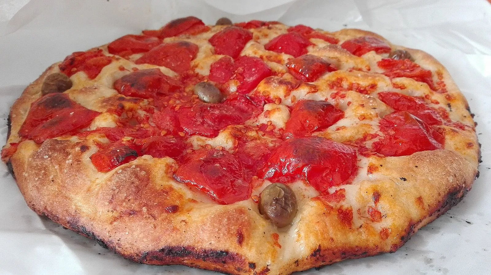 Una focaccia barese rotonda appena sfornata, condita con pomodorini e qualche oliva
