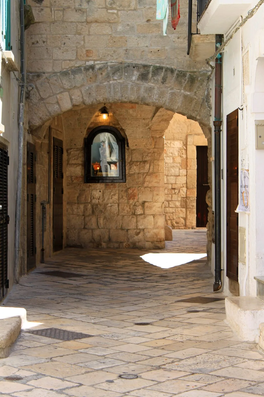 Un vicolo lastricato del centro storico di Polignano a Mare con un arco in pietra, porte in legno e un'edicola votiva illuminata