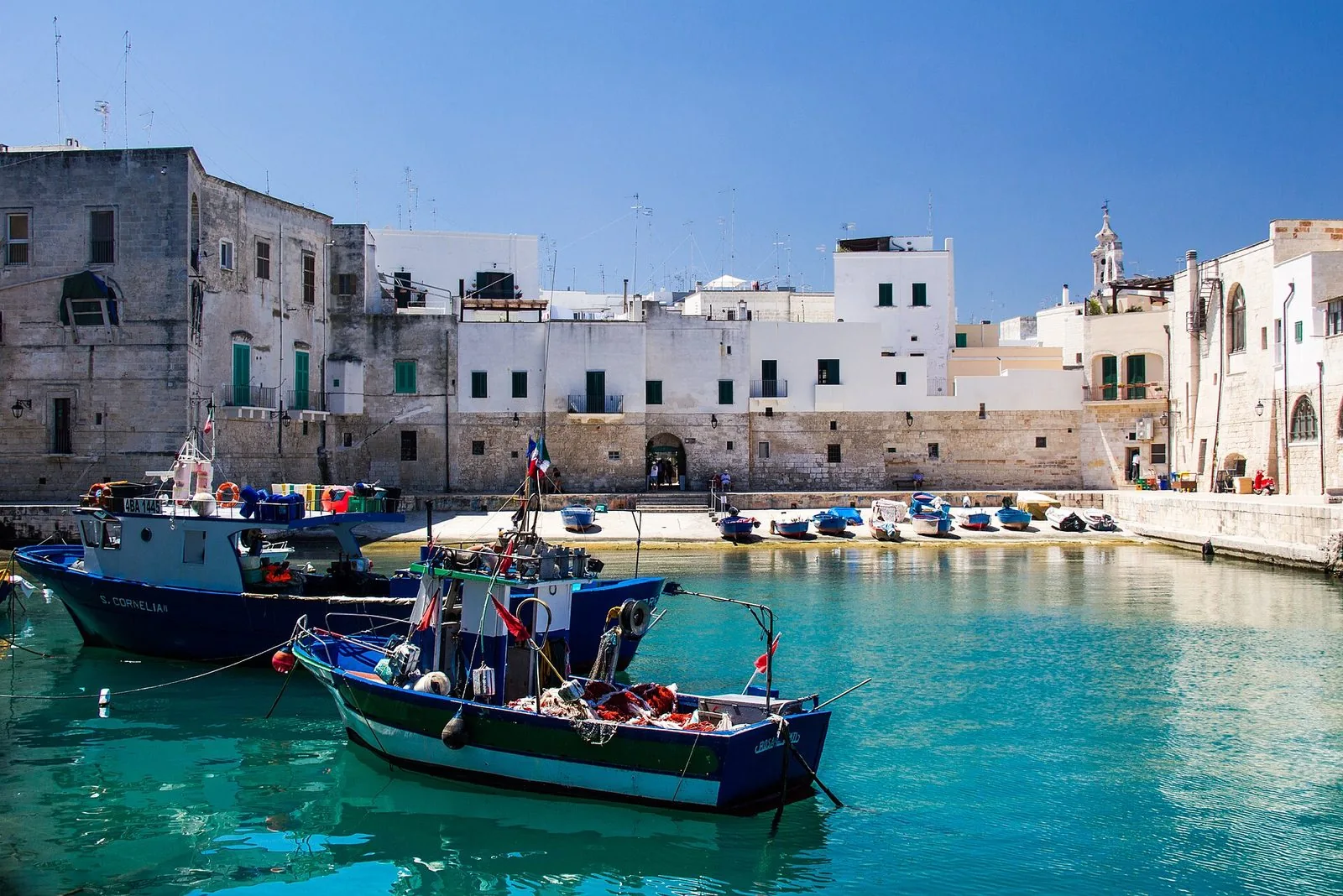 Il porto antico di Monopoli con barche da pesca blu ormeggiate nell'acqua turchese e, sullo sfondo, le case chiare del centro storico e un campanile